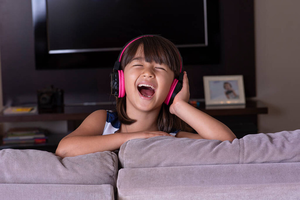 Happy cute little girl listening to music on the sofa at home - Фото, зображення