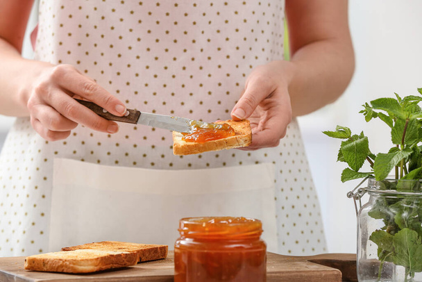 Woman spreading tasty peach jam on bread slice in kitchen - Photo, Image