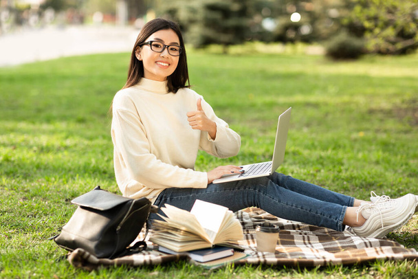 Student using laptop, sitting in the park near campus - 写真・画像