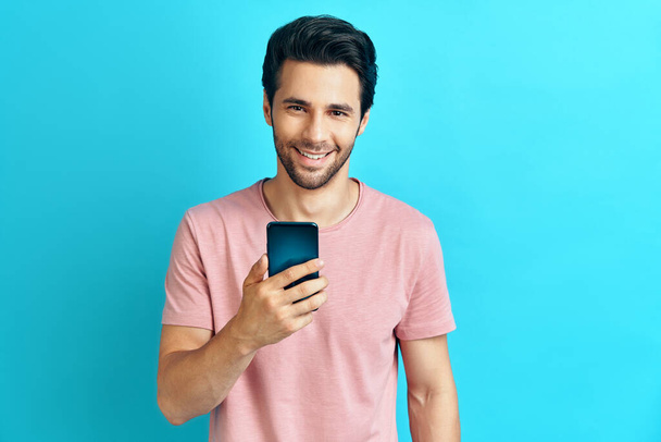 Handsome smiling man holding mobile phone and looking to camera - Fotoğraf, Görsel