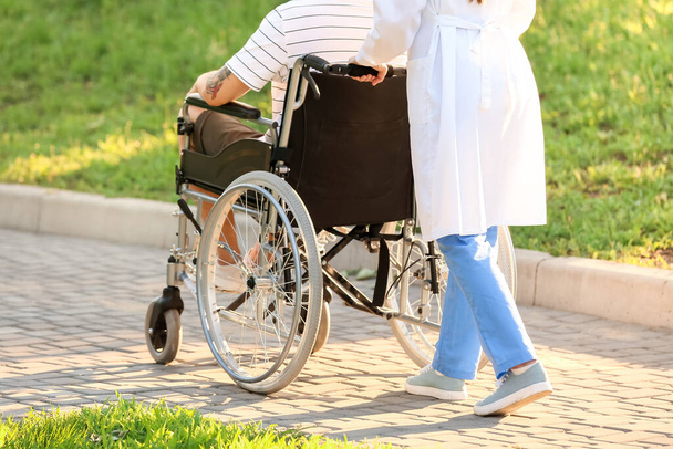 Doctor and young man in wheelchair outdoors - Foto, Imagen