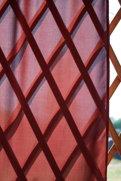 Червона хвиляста натуральна тканина завіса над дерев'яною перегородкою з бамбукових рейок, натуральний східний декор, вибірковий фокус
 - Фото, зображення