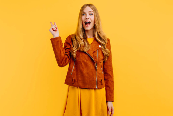 A beautiful girl points to an empty space, a girl on a yellow background, in an autumn jacket - Foto, Bild