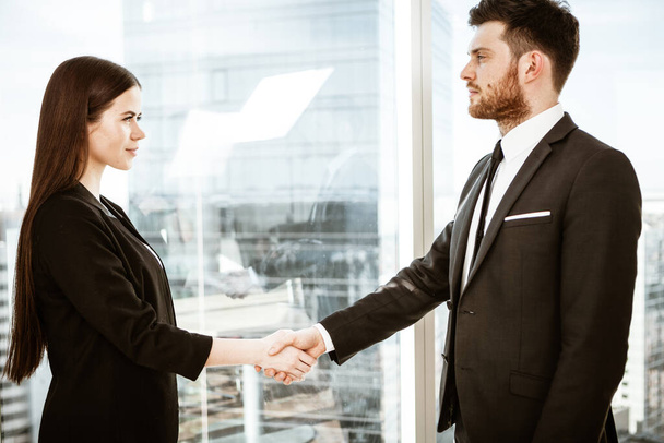 Successful business concept. Young businesswoman and businessman shake hands after signing partnership cooperation contract in office. Two managers man and woman teamwork indoors - Photo, Image