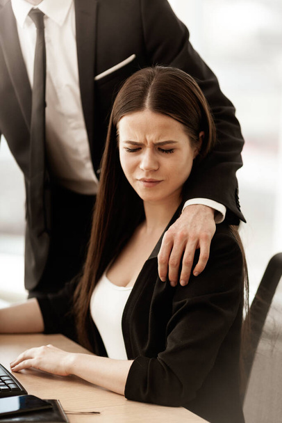 Sexuelle Belästigung am Arbeitsplatz. Männlicher Geschäftsmann legt genervten weiblichen Assistentinnen am Arbeitsplatz die Hand auf die Schulter und zeigt unangemessenes Verhalten. Zwei Männer und eine Frau im modernen Büro. - Foto, Bild