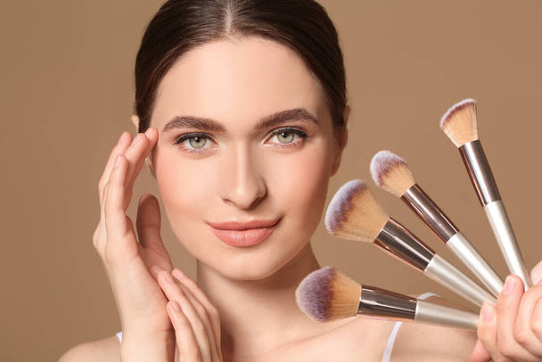 Young woman with makeup brushes on color background - Photo, Image