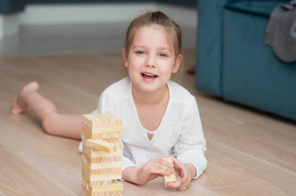 European baby girl playing on the floor, wooden blocks tower game for brain and physical Focus on the child's face. Concept of teaching children and mental skills. - Foto, imagen