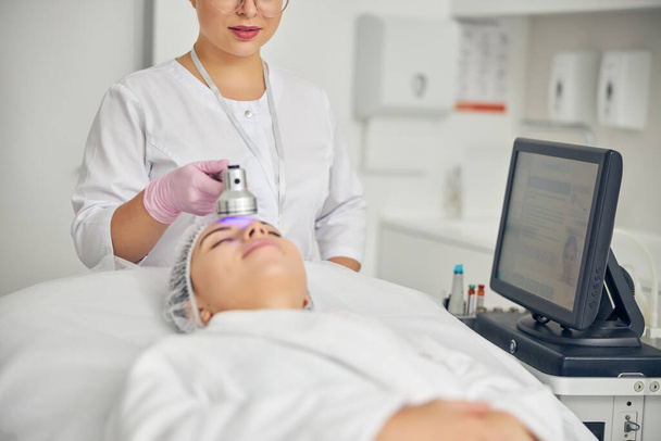 Doctor directing a photo beauty device at the patient forehead - Photo, Image