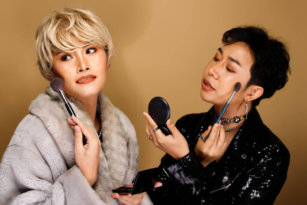 Retrato de moda 20s mujer asiática hombre tiene hermosa actualización maquillaje artista en cepillo y lápiz labial de color, usan artículos de moda, fuerte sensación posa sobre amarillo fondo aislado espacio de copia - Foto, imagen