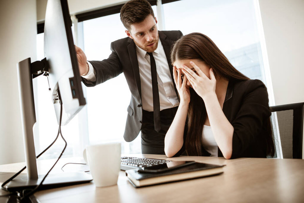 Conflict, crisis and dismissal at work. Young businessman yells at subordinate female assistant after her failure. Businessman points at monitor and fires worker. Resolving a serious work problem - Fotografie, Obrázek