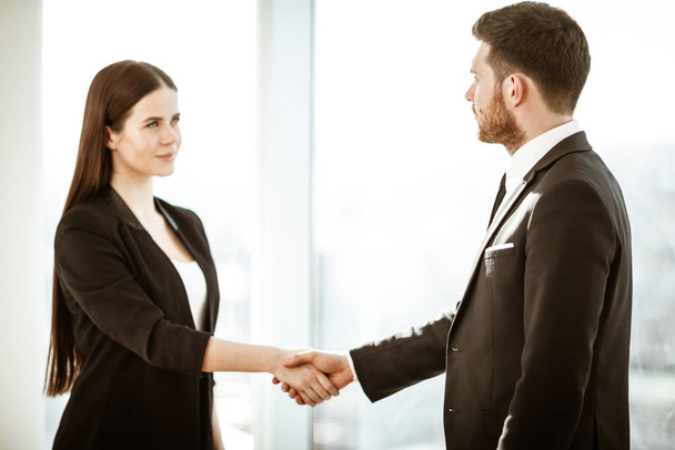 Successful business concept. Young businesswoman and businessman shake hands after signing partnership cooperation contract in office. Two managers man and woman teamwork indoors - Фото, изображение