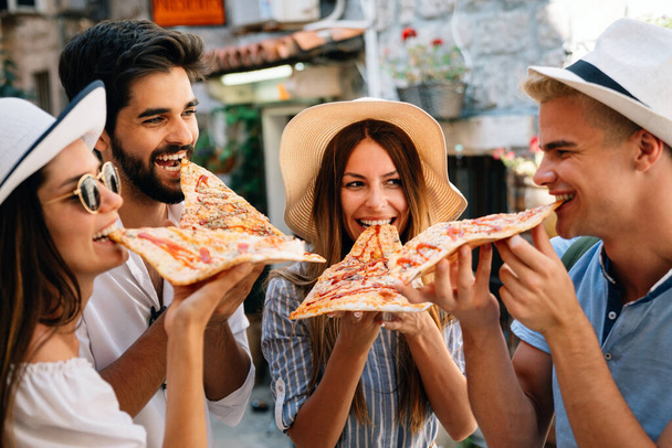 Happy group of people eating pizza outdoors, they are enjoying together. - Valokuva, kuva