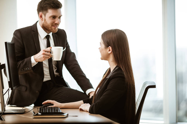 仕事での競争と関係。幸せな笑顔の男性実業家が座って職場で積極的な心の女性アシスタントに性的関心を示しています。現代のオフィスで二人の男と女の愛と同情 - 写真・画像
