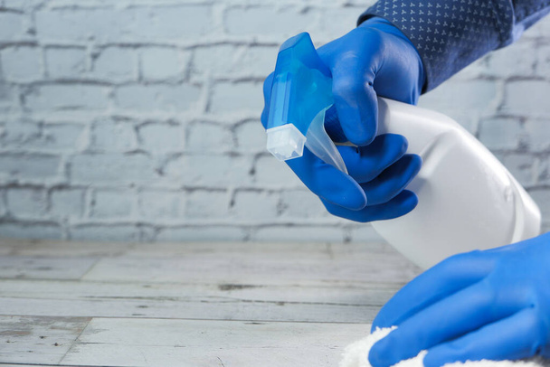 Рука людини в одноразових рукавичках, використовуючи дезінфікуючий спрей для очищення поверхні столу
 - Фото, зображення