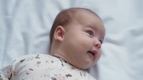 幼児期,小児期,開発,医学と健康の概念 – 近いトップビューの顔新生児裸目を覚ます活気のある遊び心のある赤ちゃんの笑顔と白い背景にベビーベッドに横たわっているおもちゃのための笑いの手の届くところ - 映像、動画