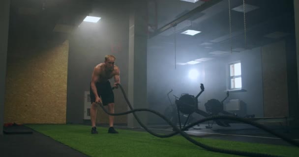 Fitness muž cvičení s bojovým lanem opuštěné skladiště. Tvrdý muž pracuje v křížovém tréninku tělocvična vyrobena uvnitř staré továrny. - Záběry, video