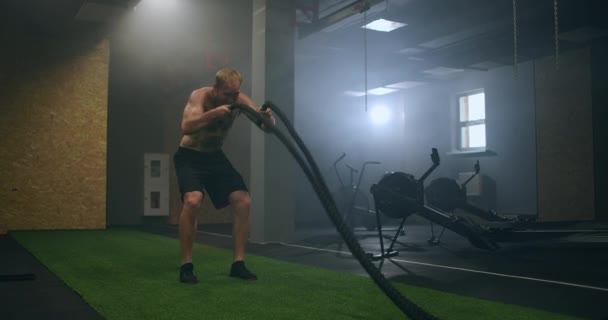 Fitness muž cvičení s bojovým lanem opuštěné skladiště. Tvrdý muž pracuje v křížovém tréninku tělocvična vyrobena uvnitř staré továrny. - Záběry, video