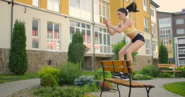 街の公園のベンチでゆっくりと女性がジャンプします。ベンチに足を踏み入れる。都市環境での訓練 - 映像、動画