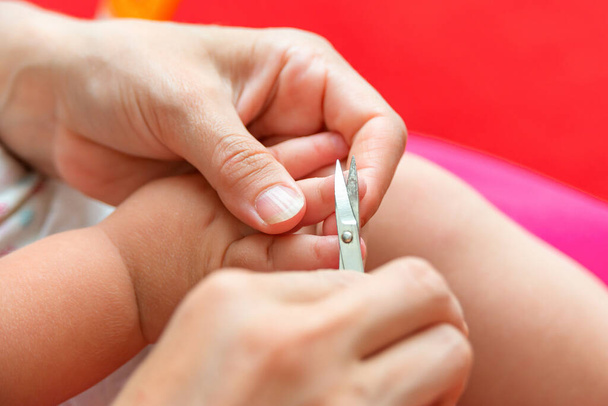 A mãe corta as unhas dos pés do bebé com uma tesoura pequena. Cuidados e tutela das crianças pelos pais
 - Foto, Imagem