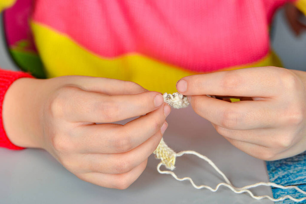 Una ragazza si siede a un tavolo e cerca di imparare a lavorare a maglia se stessa. - Foto, immagini