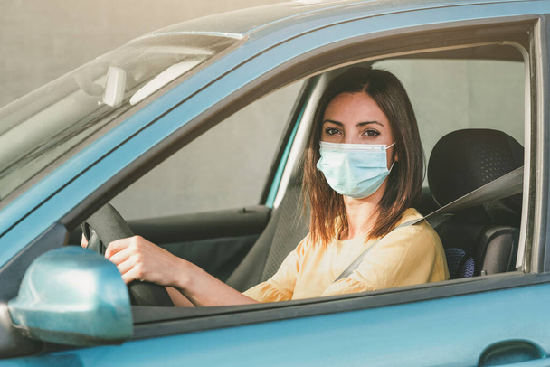 Mujer joven conduciendo coche con máscara médica en su cara al aire libre - Foto, imagen