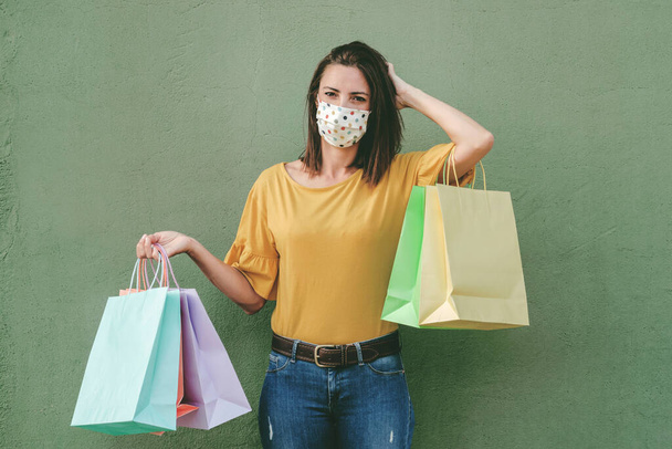 Young happy woman wearing medical mask holding a shopping bags over green backgroun - Fotoğraf, Görsel
