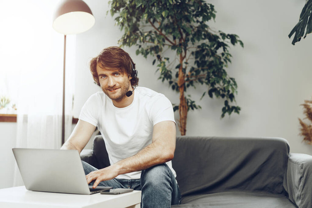 Hombre joven hombre de negocios con auriculares trabajando en el ordenador portátil desde casa - Foto, imagen