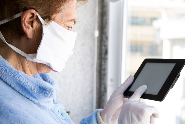 senior woman with medical mask and gloves using tablet at home. quarantine. Corona Virus health concept ordering products online - Foto, immagini