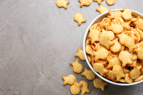 Delicious goldfish crackers in bowl on grey table, flat lay. Space for text - Foto, afbeelding