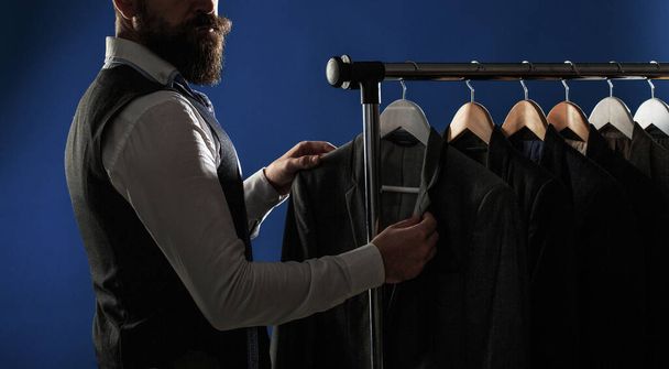 Elegant mans suits hanging in a row. Luxury man classic suits on rack in elegant mens boutique. Mens lothing, shopping in boutiques. Tailor, tailoring. Man suit, tailor in his workshop - Foto, imagen