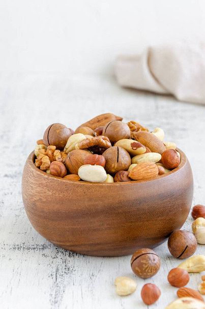 Mix of nuts in a wooden bowl on a light wooden background. Healthy food concept. Vertical, copy space - Фото, зображення