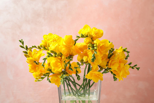 Beautiful blooming yellow freesias in glass vase against pink background - Fotografie, Obrázek