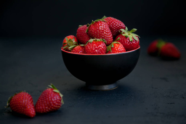 Ripe red fresh strawberries in a bowl on a black background - Фото, изображение