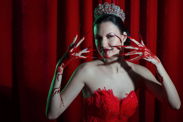 A woman vamp in a red dress, a crown with a bright manicure and blood. An image of Halloween. - Foto, imagen