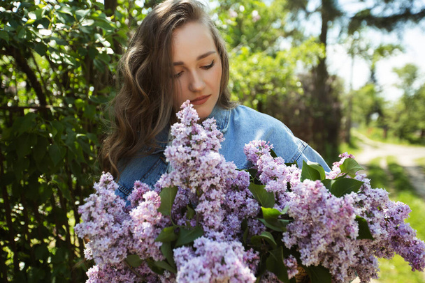 Menina bonita com flores lilás em suas mãos. Uma menina com flores lilás na primavera no parque. Uma menina com cabelo comprido. - Foto, Imagem