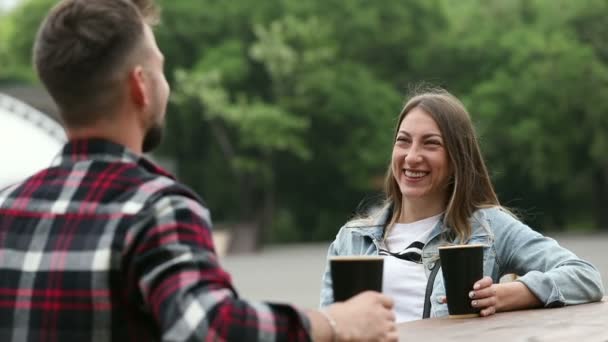 Ein junges Mädchen trinkt Kaffee und unterhält sich mit einem Mann im Park: scherzt, lacht und gibt High Five. - Filmmaterial, Video