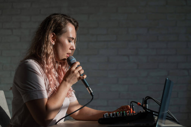 Una mujer canta en un micrófono y juega en línea. Una blogger está grabando una canción usando un sintetizador con un portátil. - Foto, Imagen