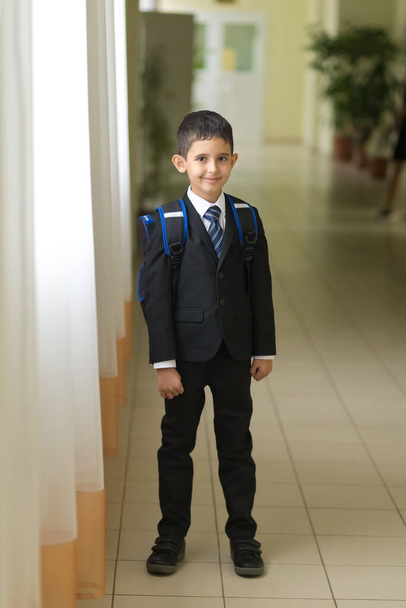 Joyeux garçon intelligent mignon en costume noir avec un sac à dos. L'enfant est prêt pour l'école. Première fois à l'école. Retour à l'école.  - Photo, image