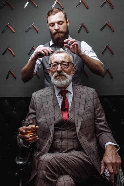 Bearded old businessman sitting at barber shop in chair choosing - Foto, Bild