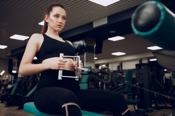 Attractive young woman doing exercises for the muscles of the arms and back in a gym - Valokuva, kuva