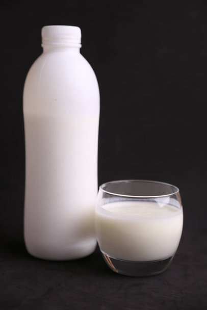 A vertical shot of a white plastic bottle and a transparent cup full of milk - Фото, зображення