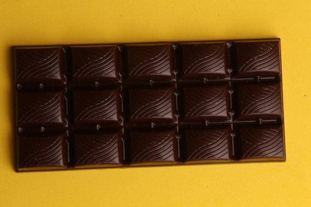 A top view of a bar of dark chocolate isolated on a yellow background - Fotoğraf, Görsel