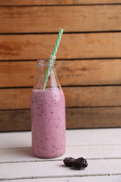 A strawberry smoothie in a bottle with frozen blackberries on the side - 写真・画像