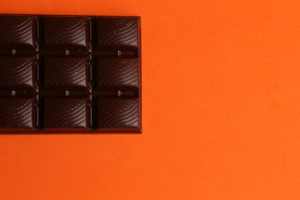 A closeup shot of a bar of dark chocolate isolated on an orange background - Photo, image