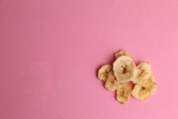 An overhead shot of dried banana chips on a pink background - Photo, Image