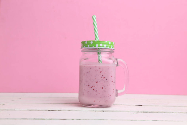 A strawberry shake on a transparent cup with green straw and cover on a pink background - Фото, зображення