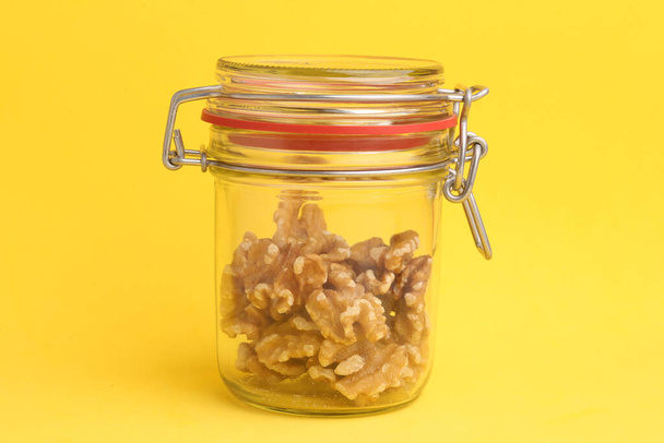 A closeup of walnut kernels inside a jar on a yellow background - Fotó, kép