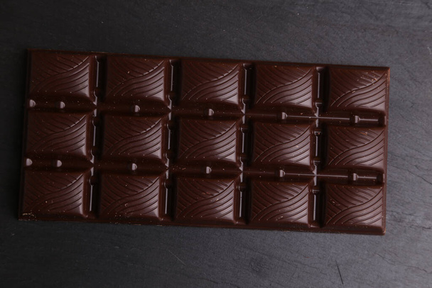 An overhead shot of a bar of dark chocolate on a black surface - Foto, afbeelding