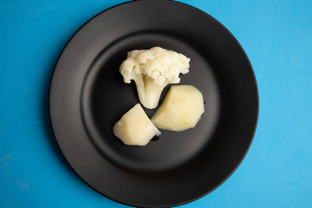 A top view of nutritious white broccoli and boiled potatoes on a black plate - Zdjęcie, obraz