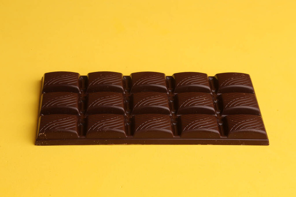 A high angle shot of a whole chocolate tablet on a yellow surface - Fotoğraf, Görsel